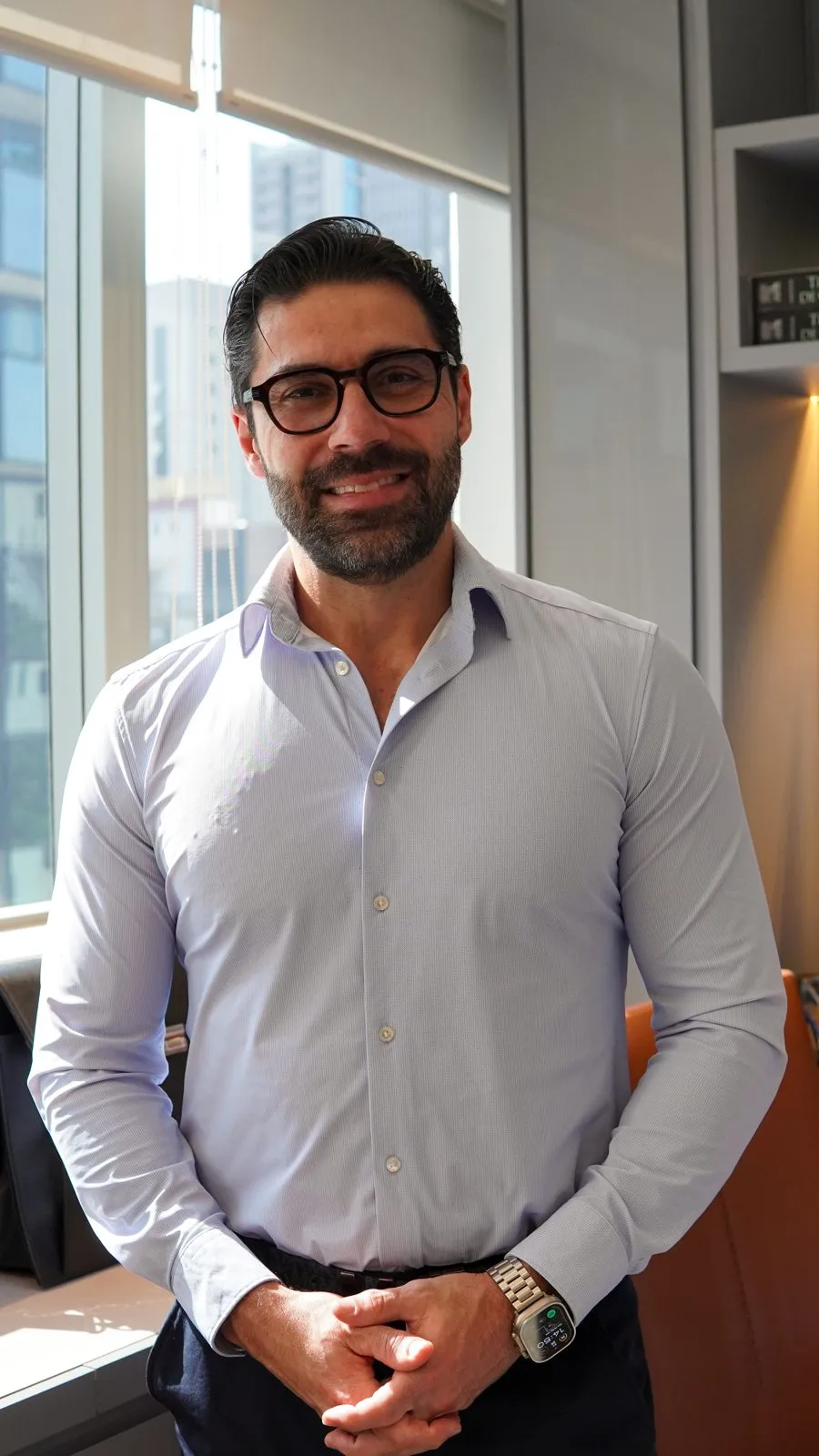 Dr. Roger Vieira in a light blue shirt, smiling at the camera with his hands together